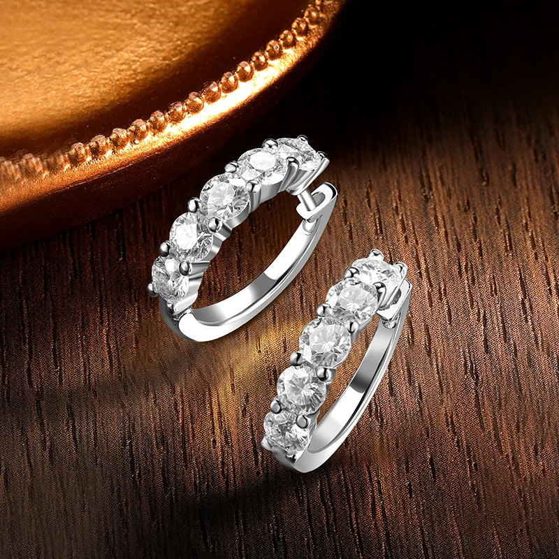 Ten-stone D-color VVS1 moissanite half-hoop stud earrings in polished white-gold 925 sterling silver, featuring a curved row of round brilliant-cut stones, displayed on a warm wooden surface with soft golden highlights.