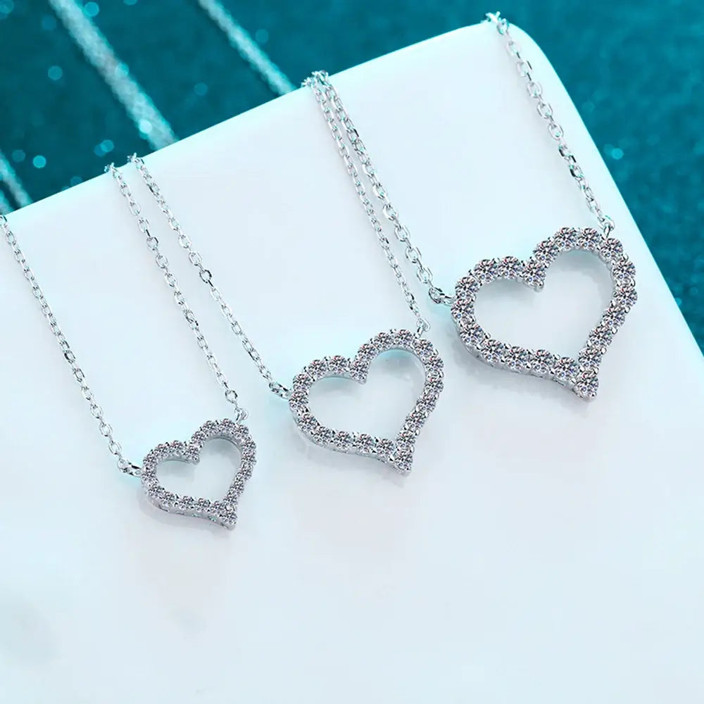 Three sparkling heart pendants on silver chains, showcasing intricate moissanite designs for women's jewelry.